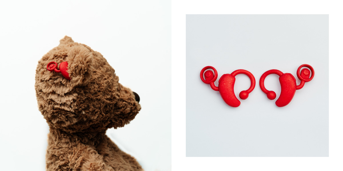 Images shows plush bear and a pair of red toy cochlear implants